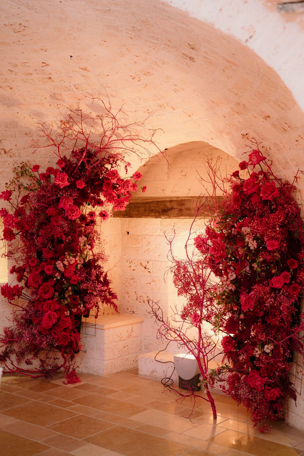 Installazione floreale LIPPOLIS: arco monumentale di rose rosse e rami in interni di trullo pugliese